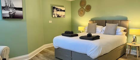 A neatly made bed with towels, a headboard, and bedside lamps in a room with green walls and wooden flooring.