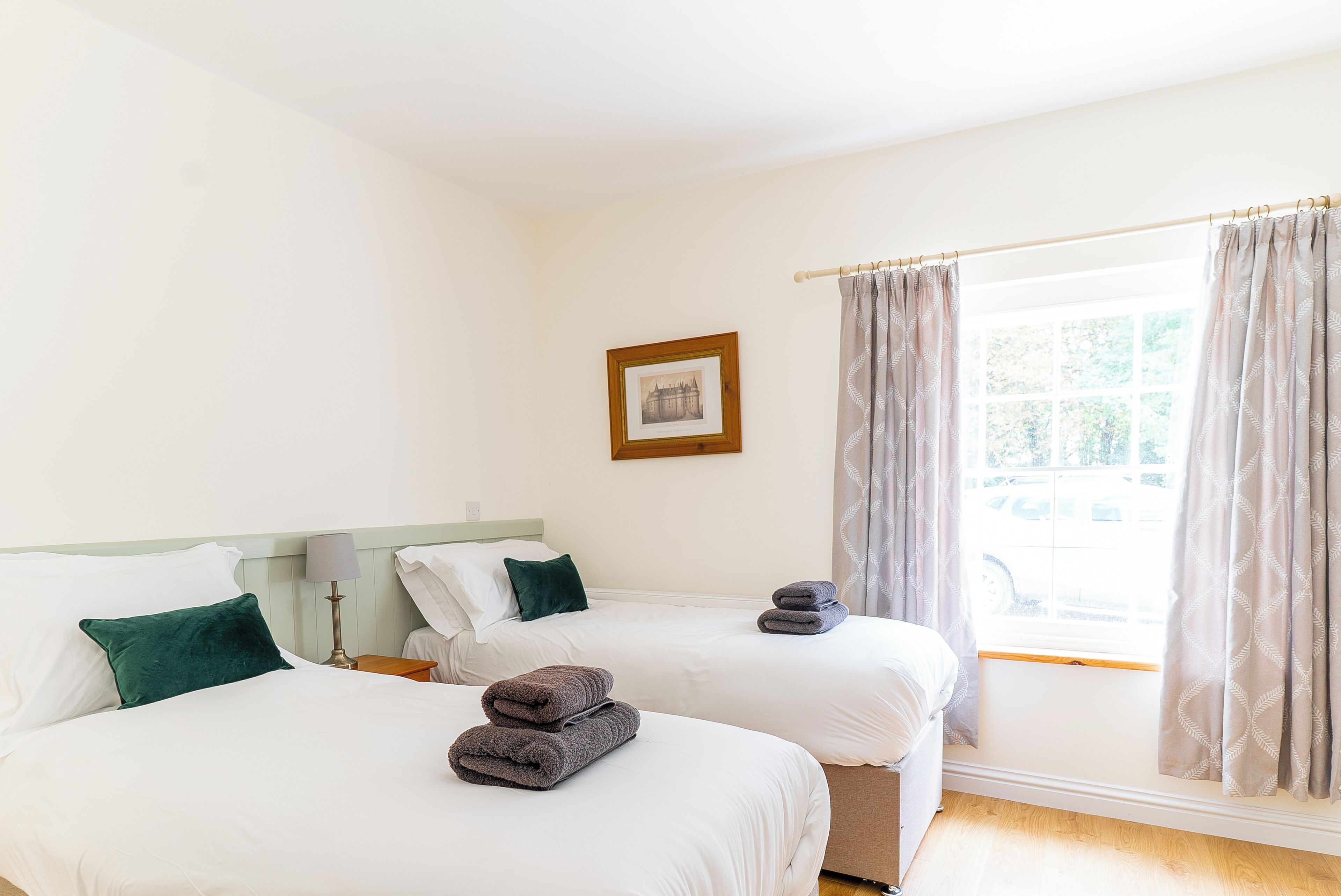A hotel room with two beds, a framed picture on the wall, and a window with curtains.