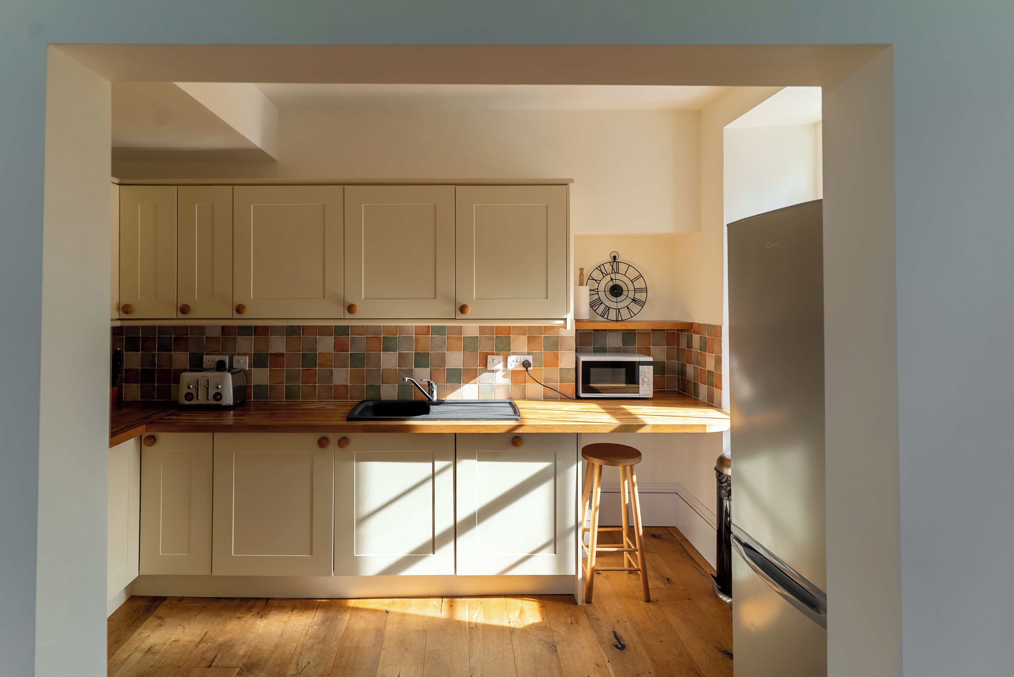 A kitchen with white cabinets, a wooden countertop, a toaster, a sink, a microwave, and a stool.