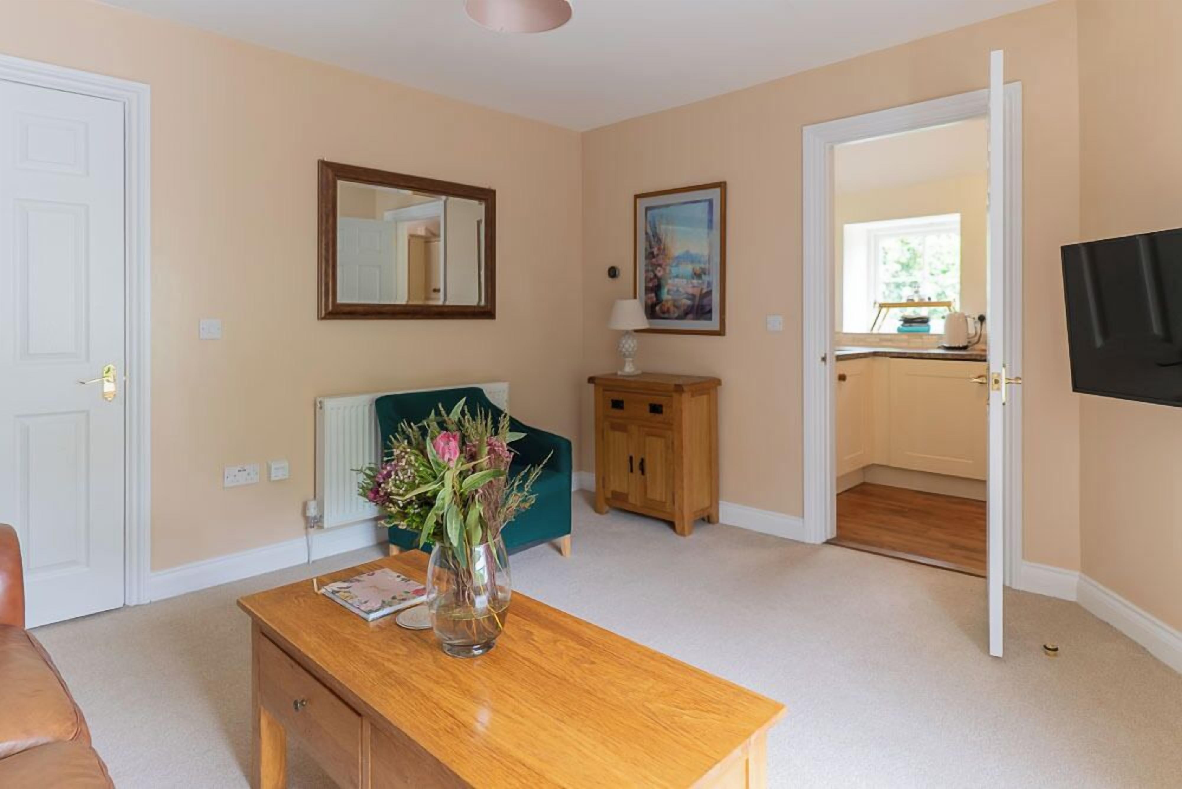 A room with a wooden table, a vase of flowers, a mirror, a painting, and a view into the kitchen.