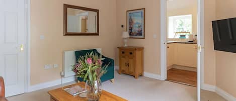A room with a wooden table, a vase of flowers, a mirror, a painting, and a view into the kitchen.