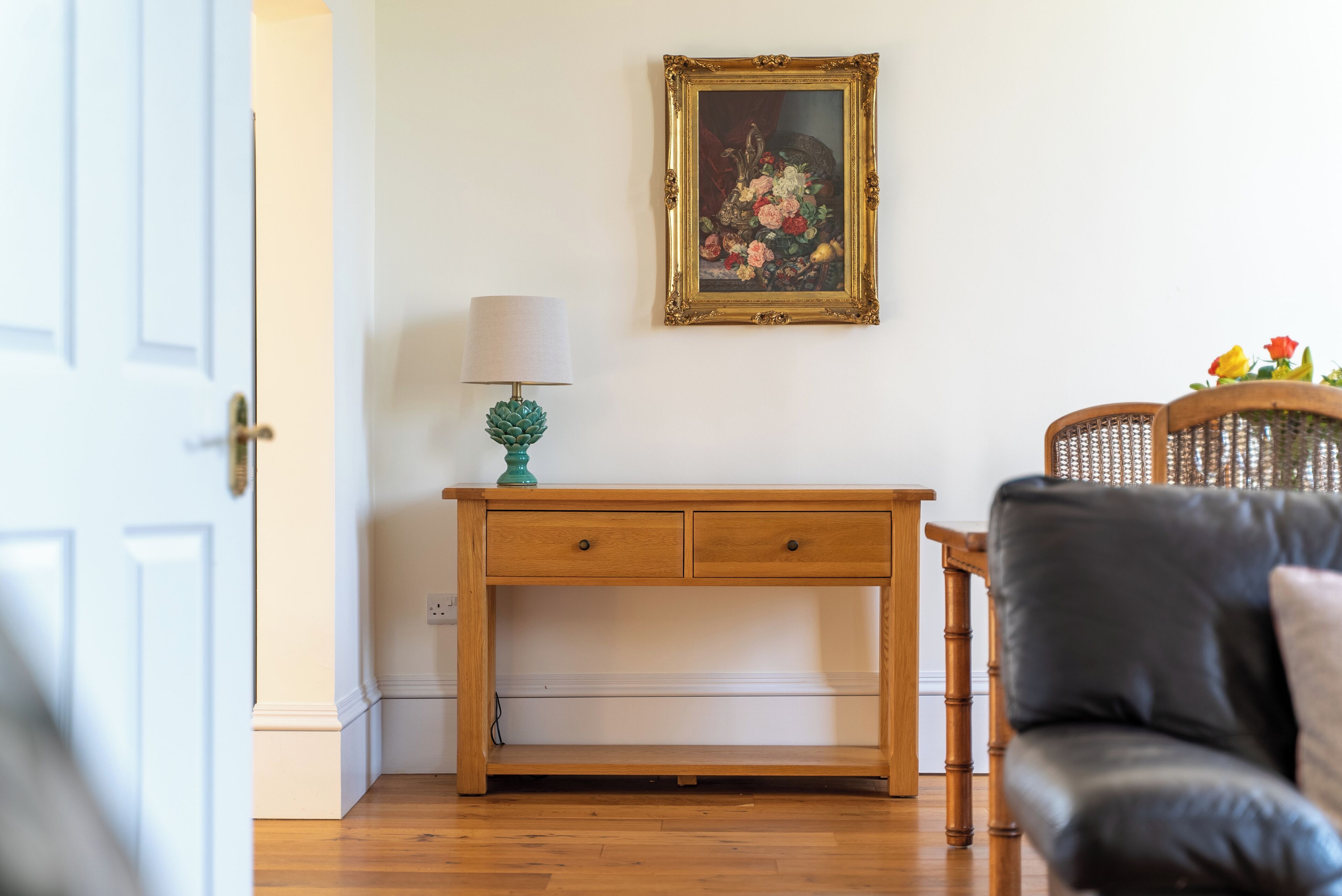 A room with a wooden desk, a lamp, a framed painting, and a leather chair.