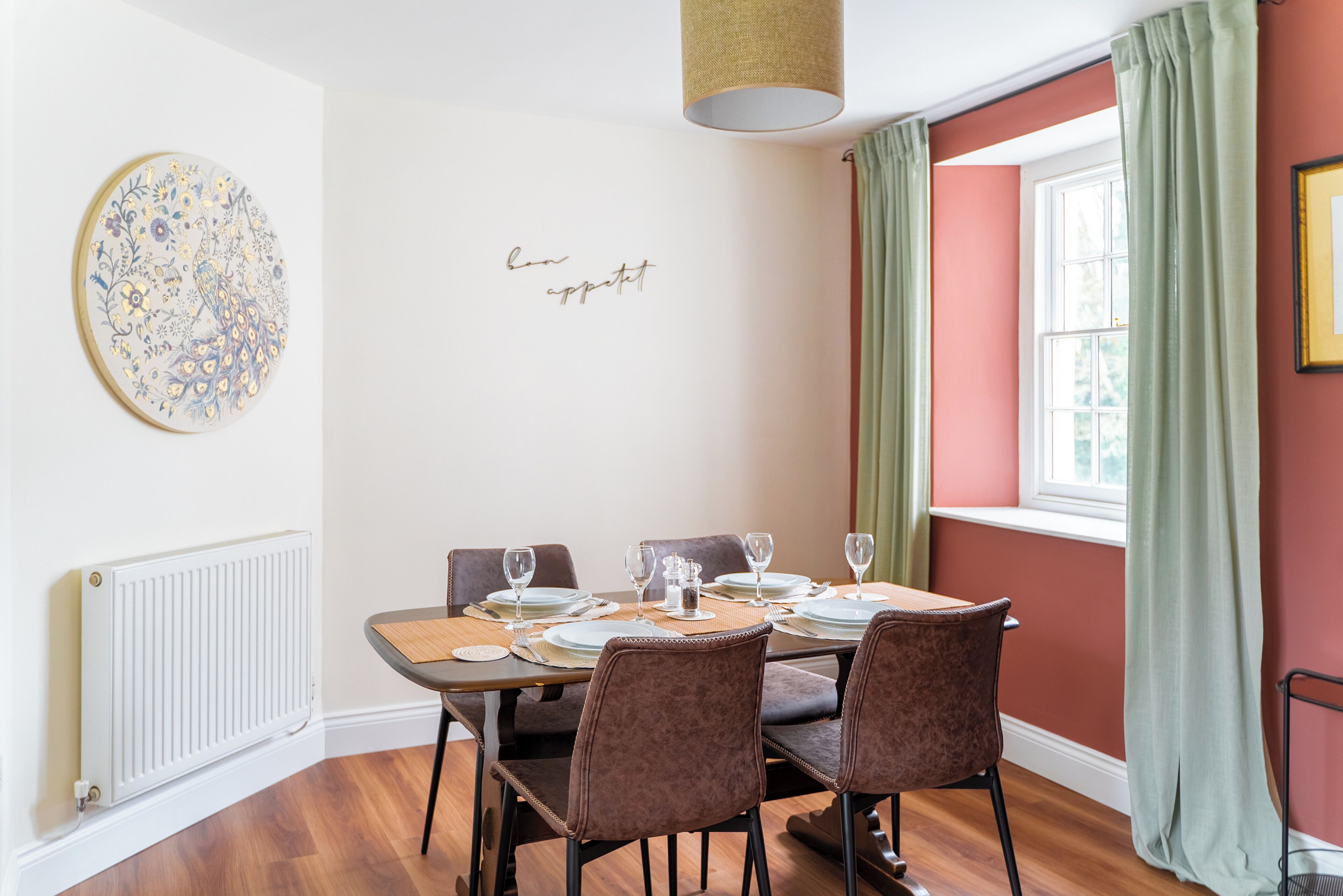 A dining area with a table set for four, chairs, a decorative wall piece, and a window with curtains.
