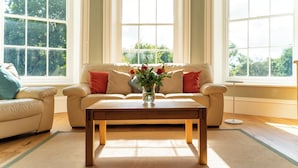 Un salón con un sofá color beige, una mesa de centro de madera y un jarrón con flores.