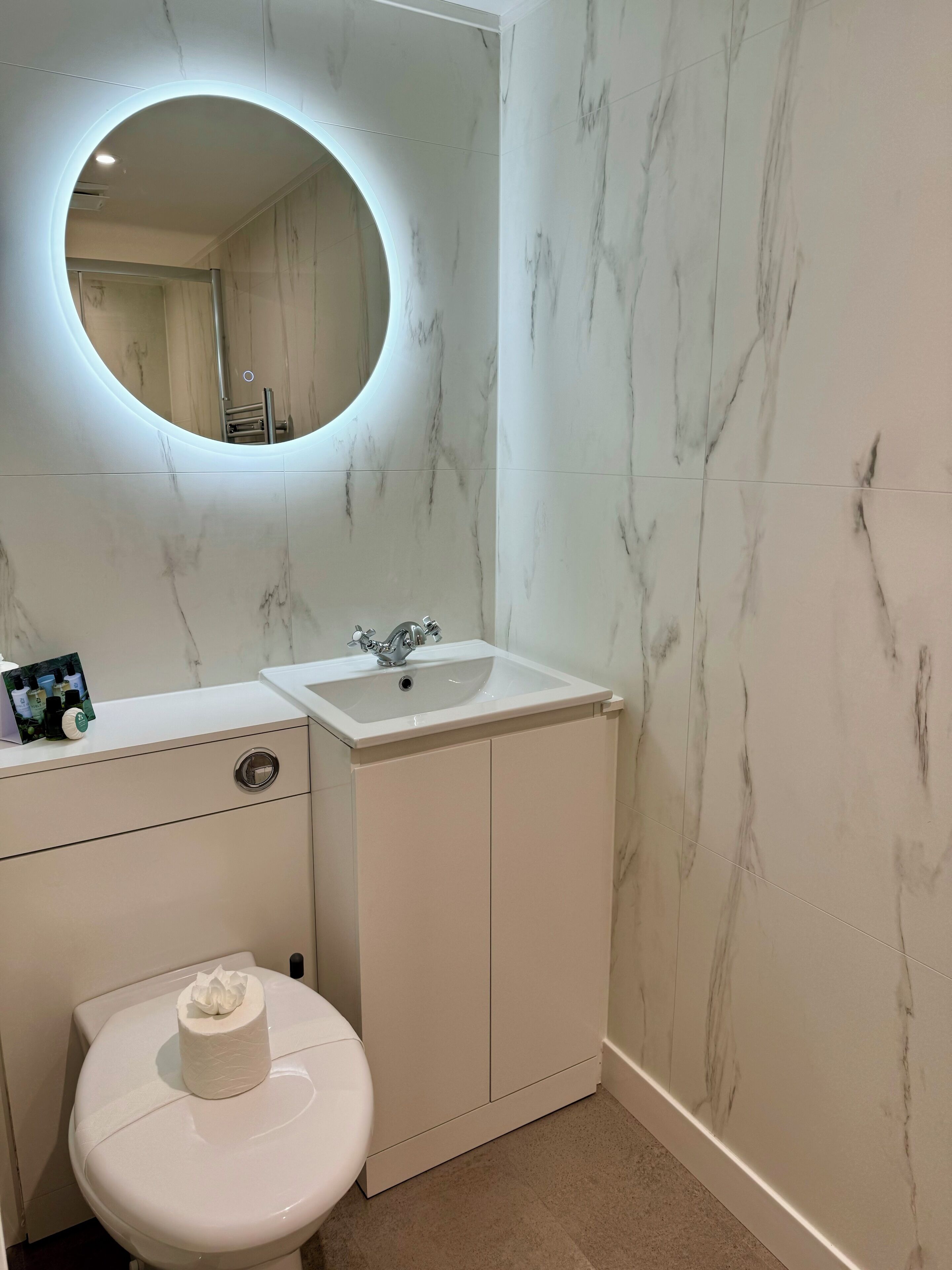 A bathroom with a white toilet, a sink with a mirror above it, and marble-patterned walls.