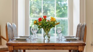 Una mesa de comedor dispuesta con platos, vasos y un jarrón con flores.