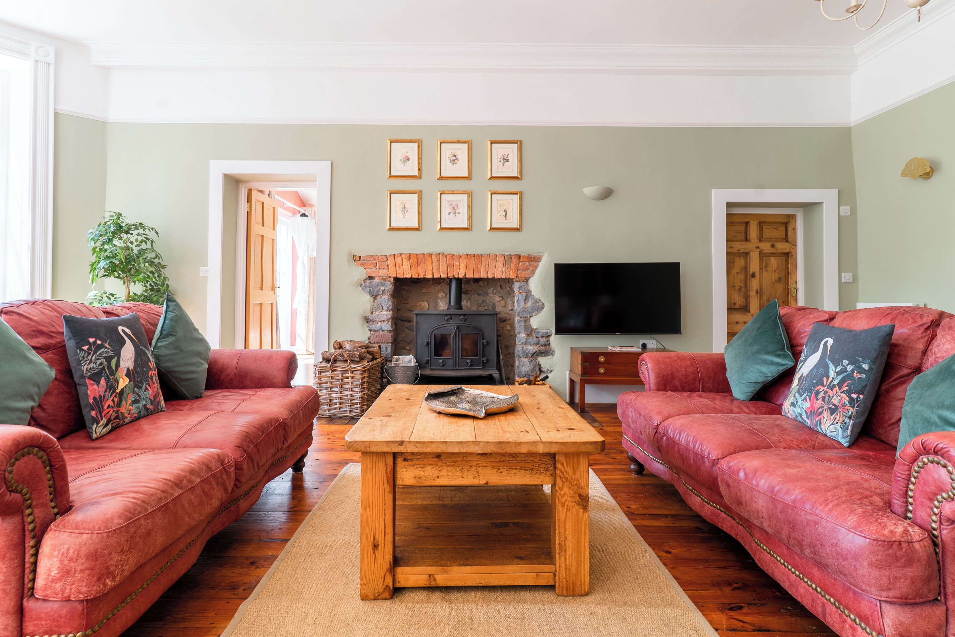 A living room with two red leather sofas, a wooden coffee table, a stone fireplace, and a flat-screen TV.
