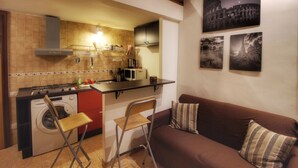 A compact kitchen with a washing machine, a dining area with a brown sofa and striped pillows, and a wall with three black-and-white photographs. - Hidden Treasure-Campo de' Fiori (Rome)