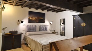 A bedroom with a bed, a wooden bench, a desk, a wardrobe, and a cityscape painting on the wall. - Hidden Treasure-Campo de' Fiori (Rome)