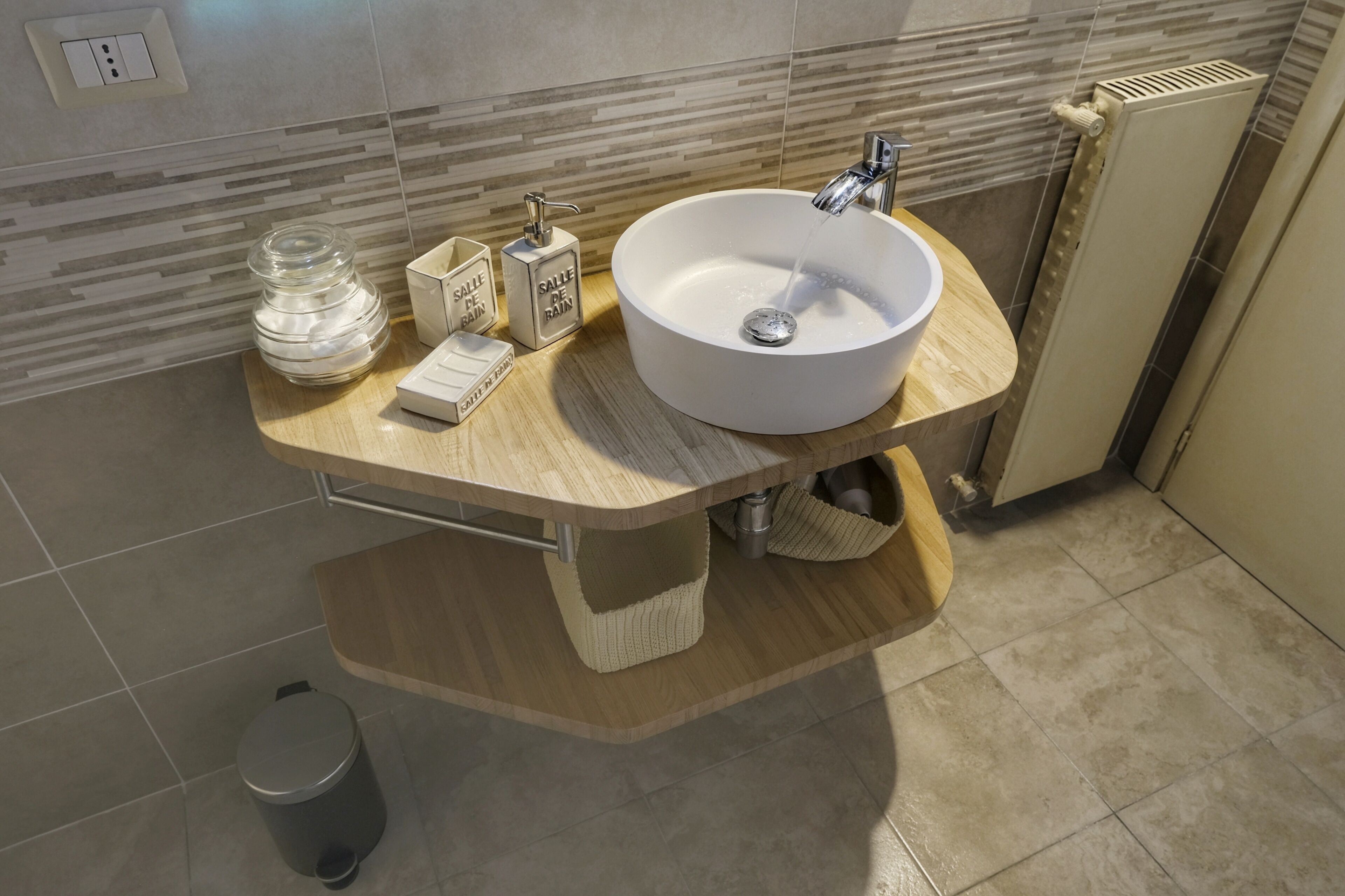 A modern bathroom with a curved wooden vanity, a white sink, and a towel rack.