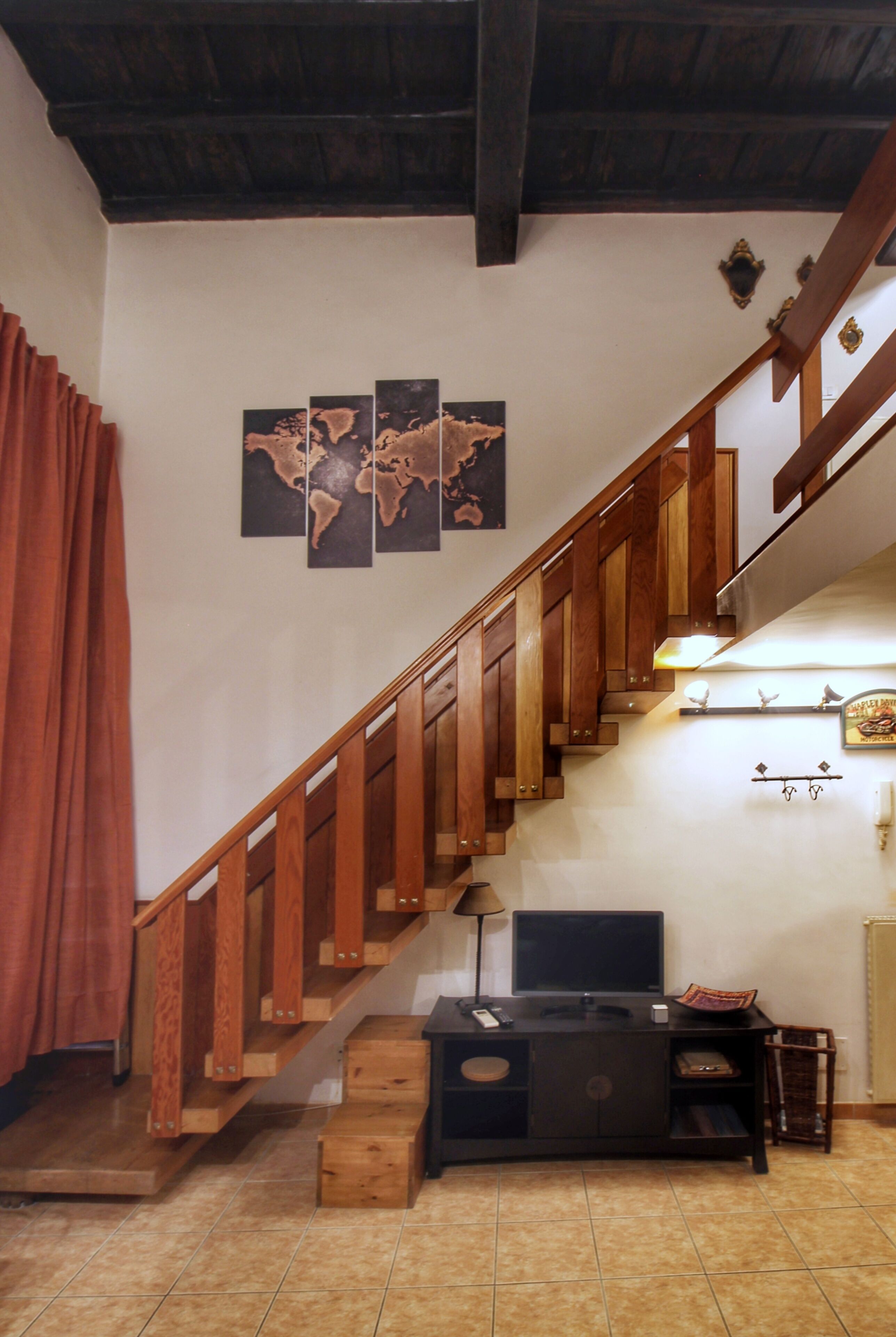 A wooden staircase with a dark finish, a flat-screen TV on a black stand, and a world map artwork on the wall.