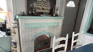 A dining area with a white brick fireplace, a blue table with a floral pattern, and white chairs. - North Coast Cottage. Located on the southern shore of Lake Ontario.  (Ransomville)