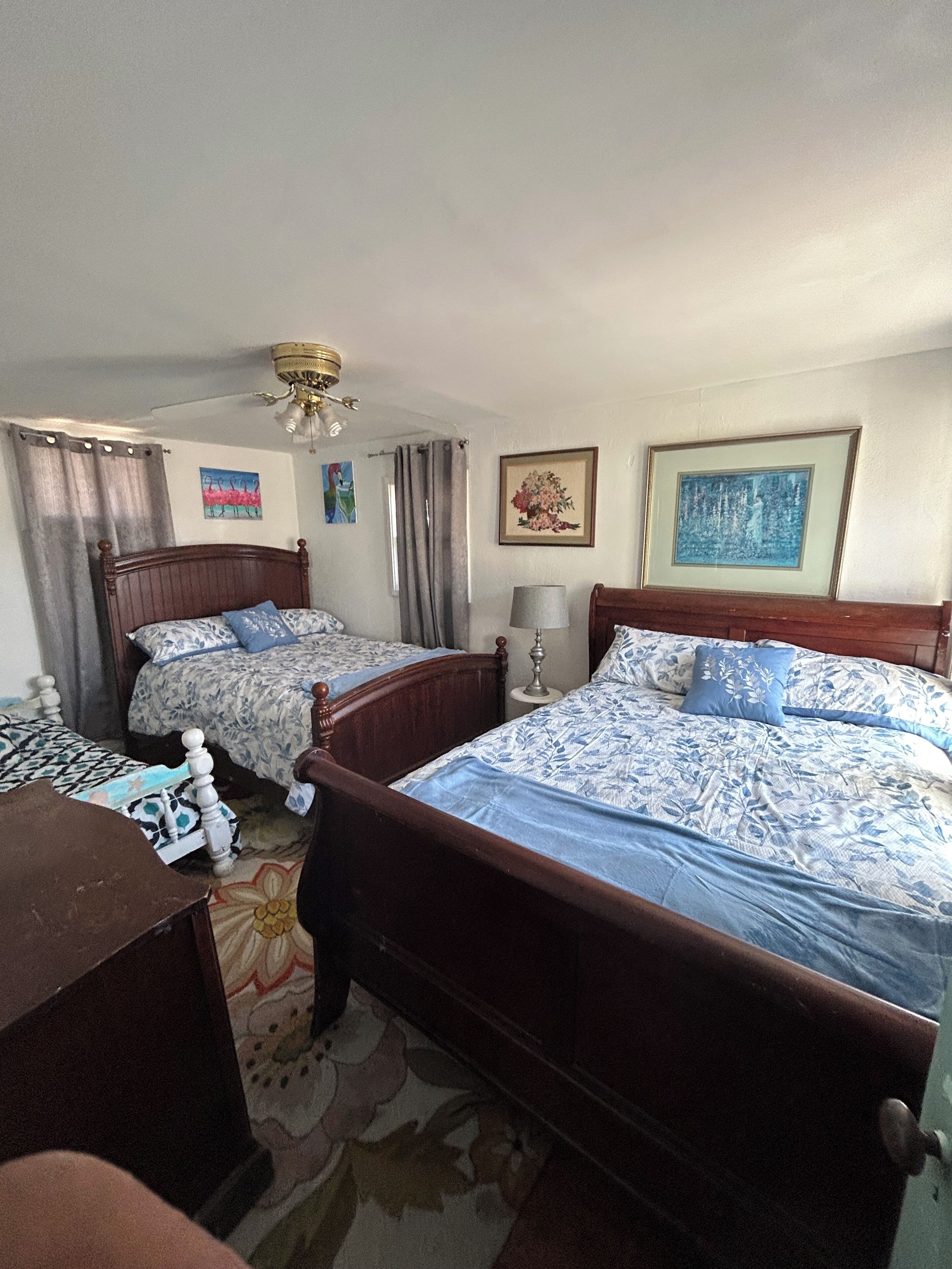 A hotel room with two wooden beds, a desk, a chair, a lamp, and a ceiling fan.