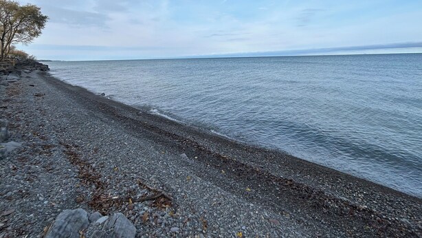 A pebbled beach with a clear sky and calm sea. - North Coast Cottage. Located on the southern shore of Lake Ontario.  (Ransomville)