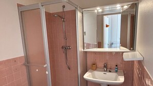 A bathroom with a glass-enclosed shower, a pedestal sink, and a mirror above the sink.