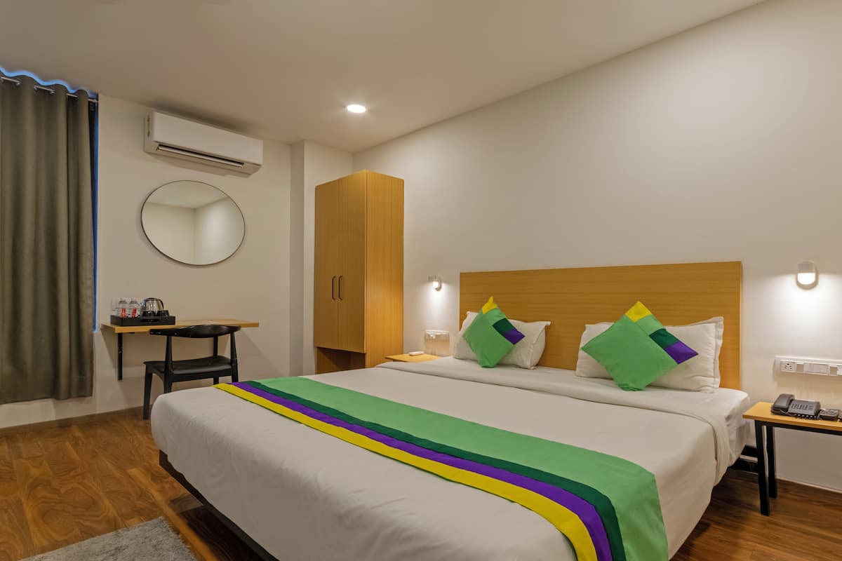 Habitación de hotel con cama, mesitas de noche, escritorio, silla, espejo y aire acondicionado.
