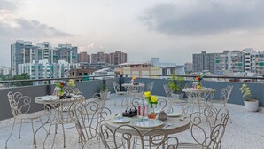 Eine Dachterrasse mit Sitzgelegenheiten im Freien, Blick auf die Stadtlandschaft und einen klaren Himmel.