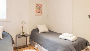 Een nette, kleine kamer met twee bedden, een tafeltje met een lamp en een schilderij aan de muur.