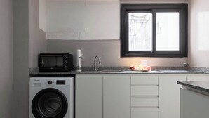 Een praktische keuken met een wasmachine, een magnetron, een spoelbak en een raam.