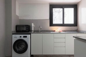 Una cocina funcional con lavadora, microondas, lavamanos y ventana.