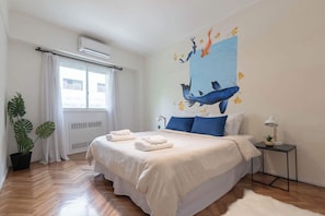 A bedroom with a bed, a nightstand, a potted plant, and a wall mural.