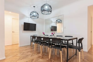 A dining area with a long table, black chairs with wooden legs, and three geometric pendant lights.