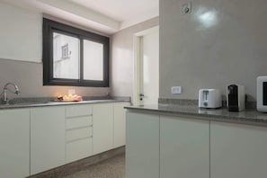 A kitchen with white cabinets, a granite countertop, a window with a black frame, a toaster, and a coffee maker.