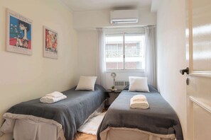 Una habitación con dos camas, toallas blancas, una ventana con cortinas, aire acondicionado y dos carteles en la pared.