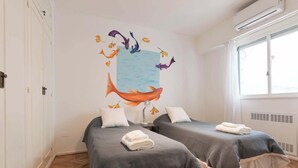 Een kamer met twee bedden, een groot wanddecoratie van vissen en een raam met uitzicht.