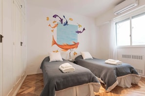 A room with two beds, a large wall mural of fish, and a window with a view.
