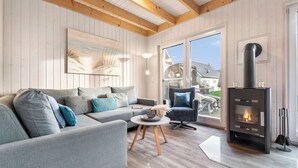 En moderne stue med en grå sofa, et rundt sofabord og en sort brændeovn.