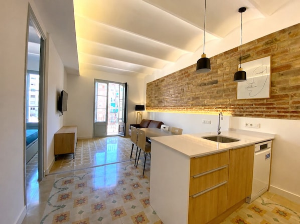 A modern kitchen with a central island, pendant lights, a brick accent wall, and a patterned floor.