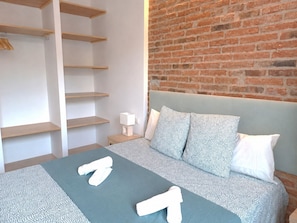 A bedroom with a bed, a brick wall, and wooden shelves.
