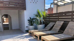 Una terrazza panoramica sul tetto con poltroncine in legno, piante in vaso e vista sulla città.