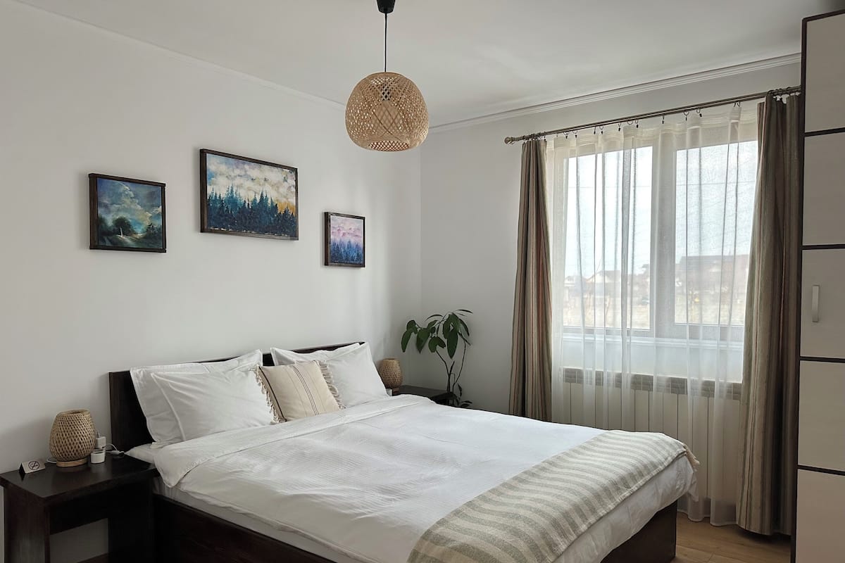 A bedroom with a large bed, a bedside table, a hanging light fixture, and three framed pictures on the wall.