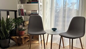 A modern living room with two grey chairs, a small round table, and a bookshelf filled with books and plants.