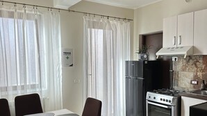 A modern kitchen with a stove, refrigerator, and cabinets. There is a dining table with chairs and a rug on the floor.