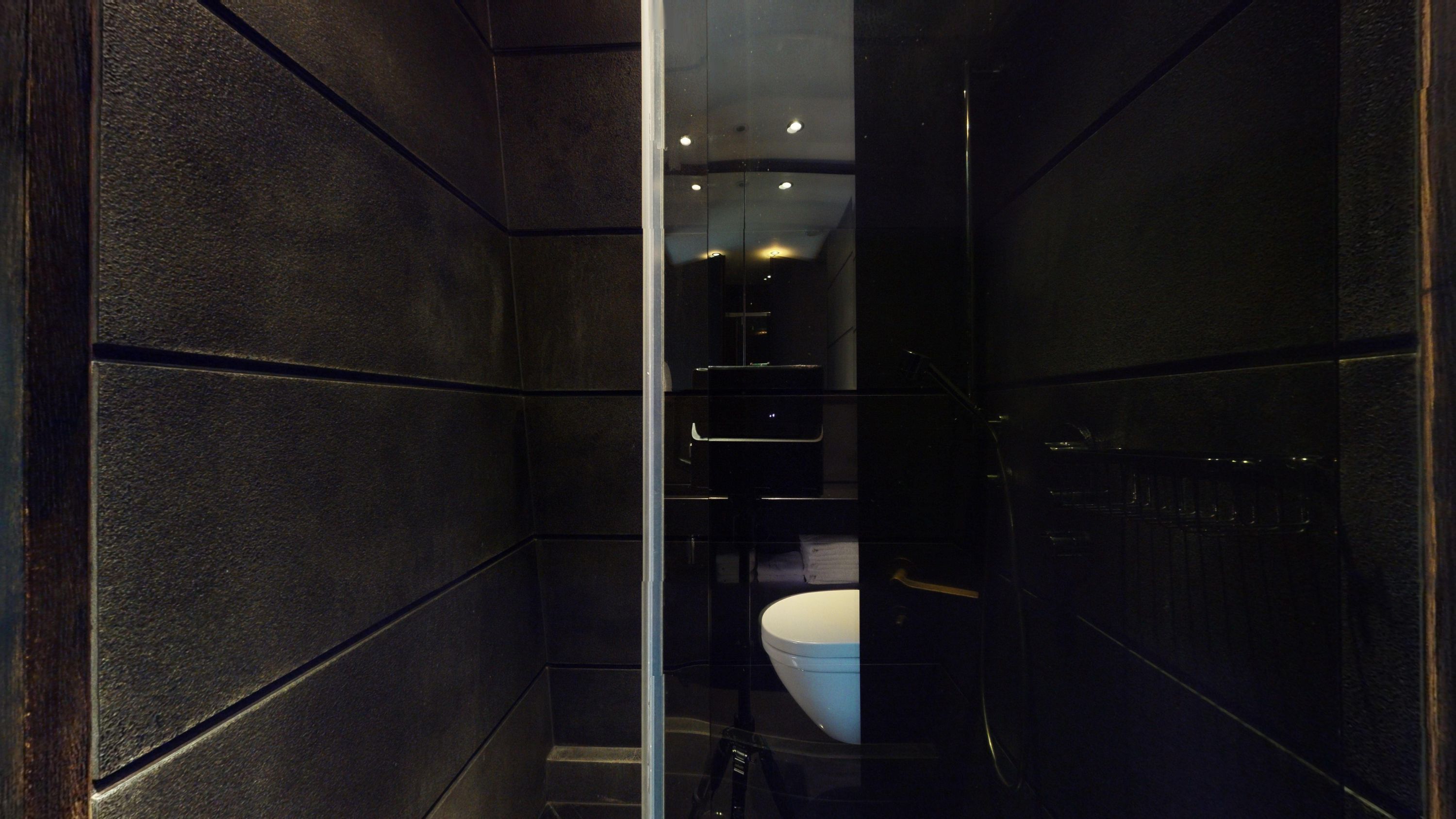 A modern bathroom with dark walls, a glass shower enclosure, and a white sink.