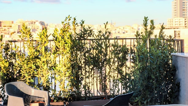 A hot tub with a waterfall feature, surrounded by outdoor seating and greenery, overlooking a cityscape. - Isabella Suites (Gzira)