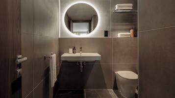 Een moderne badkamer met een ronde spiegel, een wastafel, toilet en een handdoekrek.