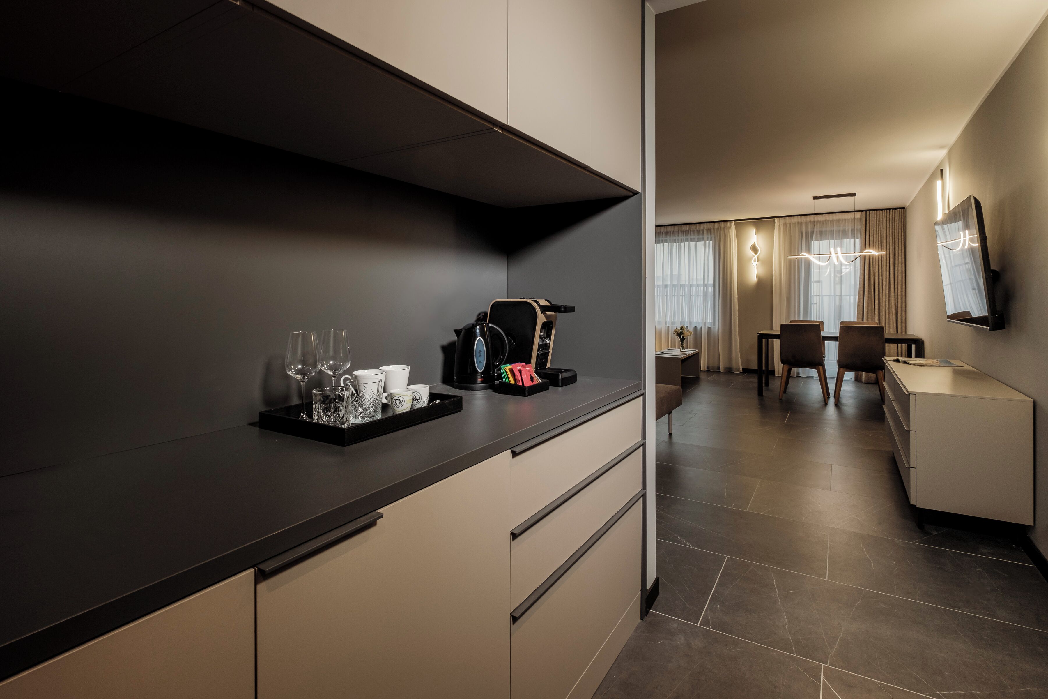 Una cocina moderna con encimera oscura, cafetera y bandeja con vasos y tazas.
