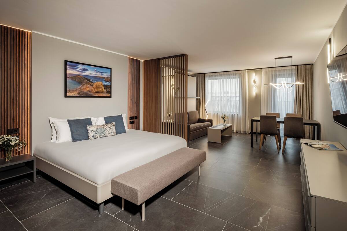 Ein modernes Hotelzimmer mit einem großen Bett, einem Schreibtisch, einer Couch und einem Essbereich.