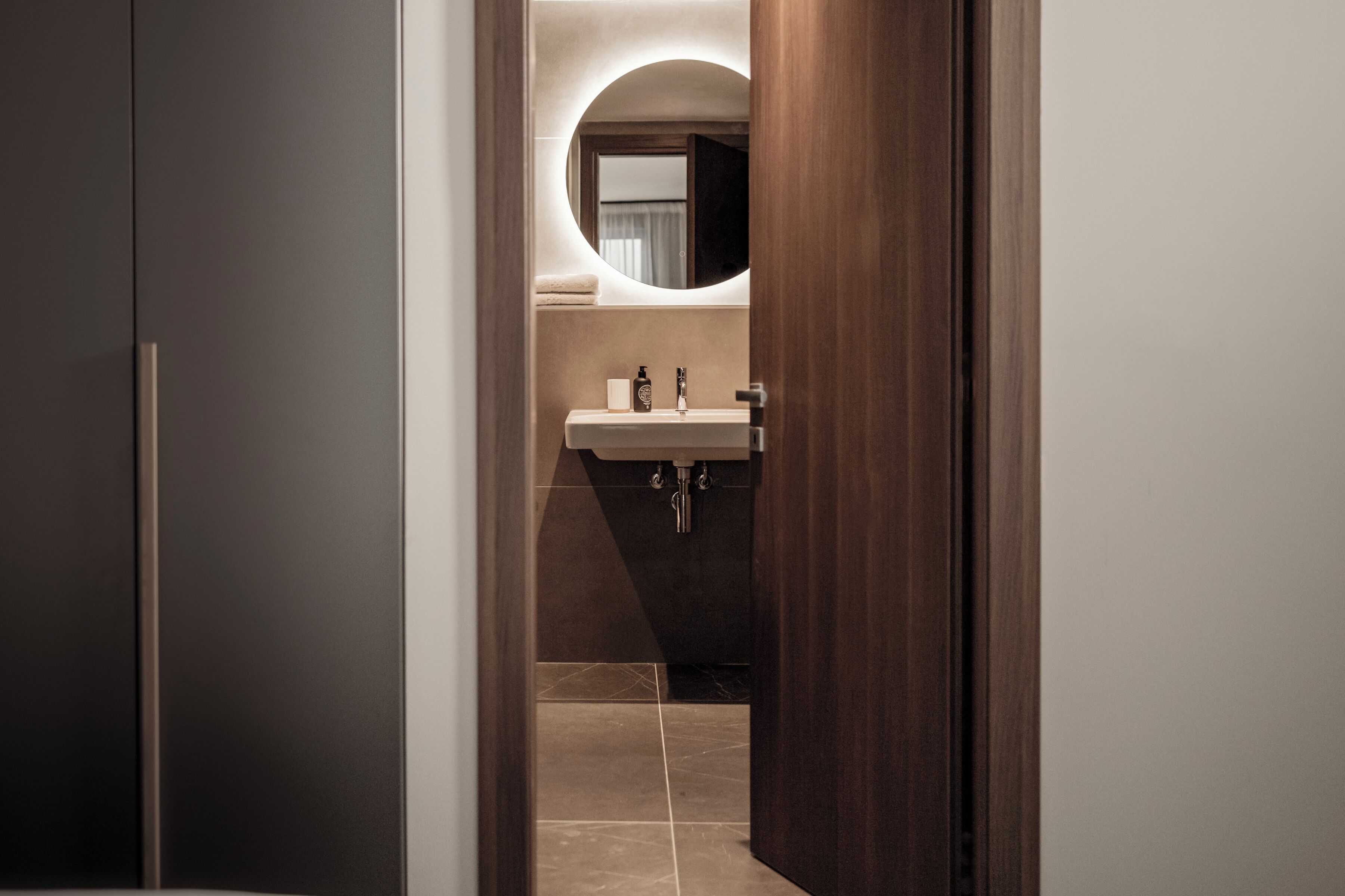 A modern bathroom with a round mirror, a sink, and a toilet.