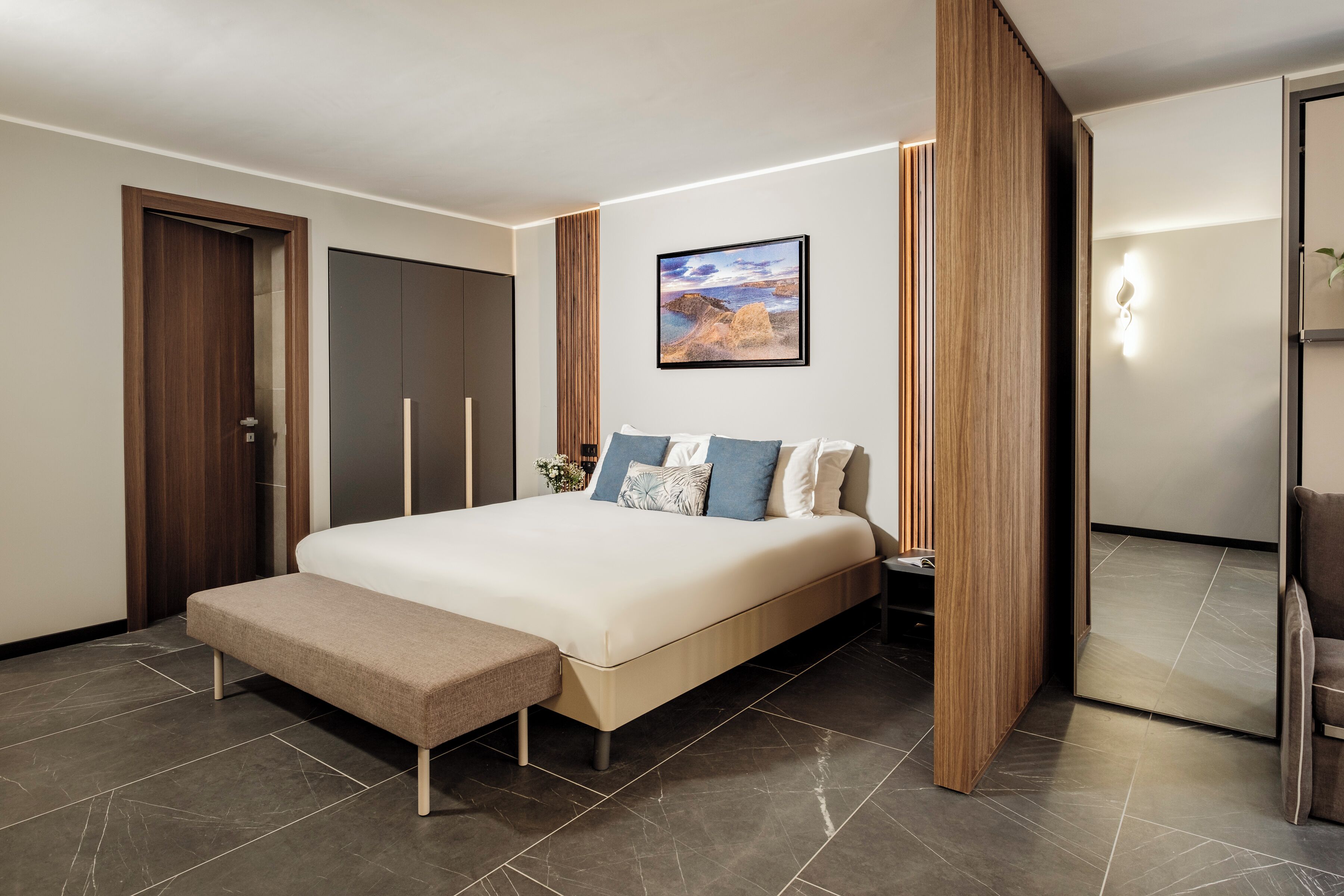 A modern bedroom with a large bed, a bench, and a wooden partition.