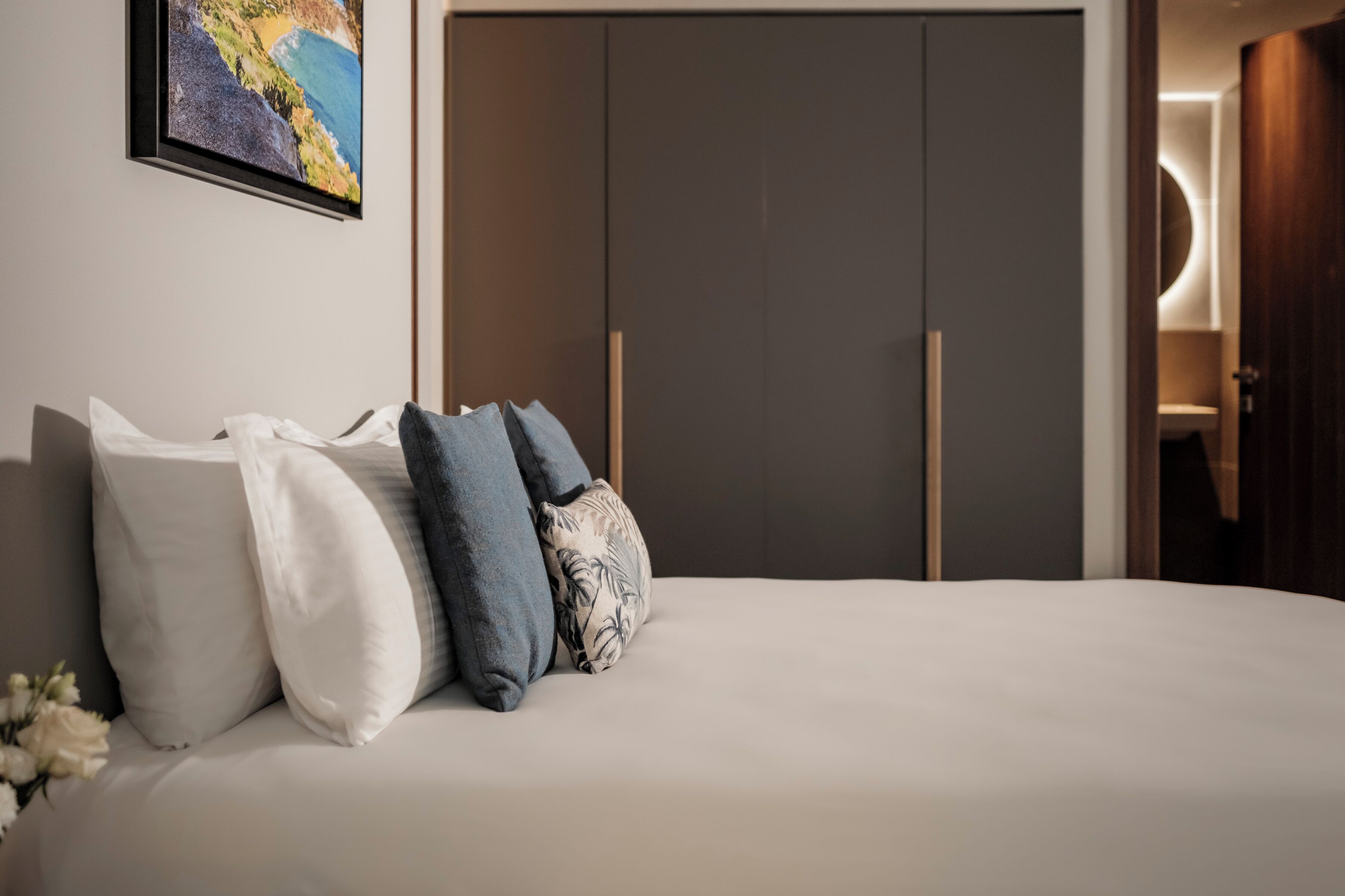Un dormitorio con cama, almohadas, un cuadro enmarcado en la pared y un armario.