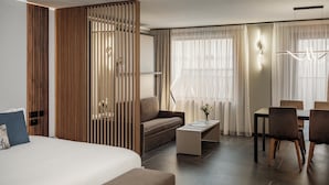 A modern hotel room with a large bed, a sofa, a dining table with chairs, and a decorative partition. - Isabella Suites (Gzira)
