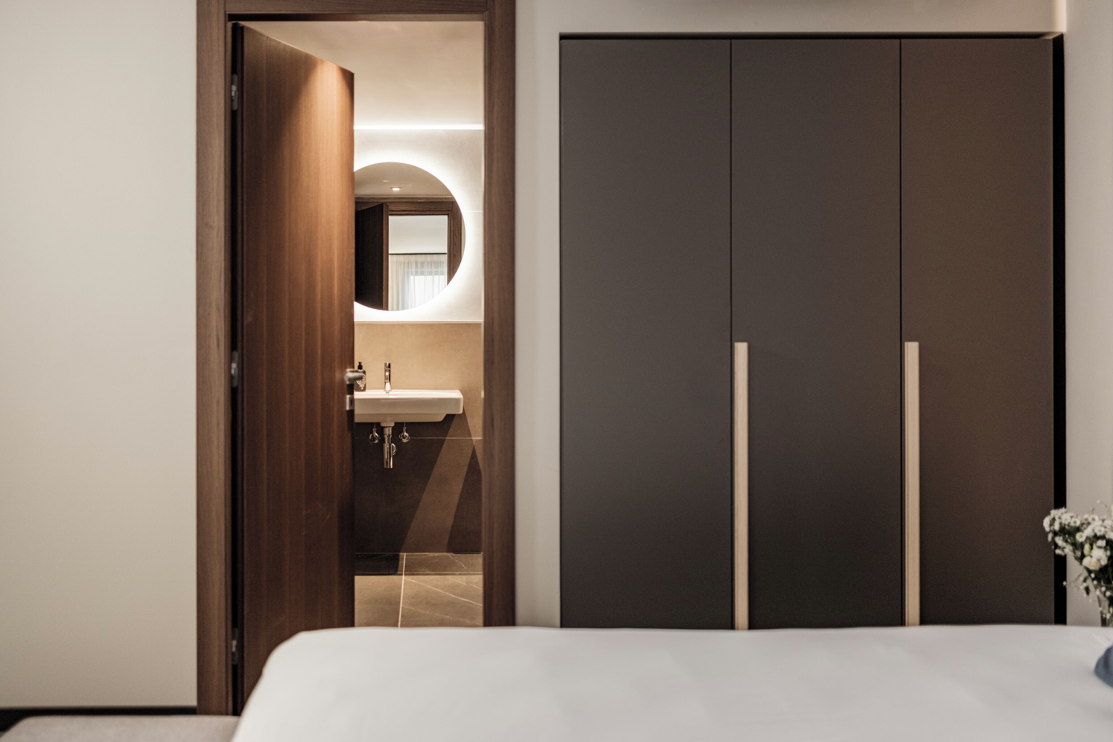 Un dormitorio con una cama, una puerta de madera, un espejo y un armario oscuro.