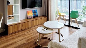 A modern living room with a flat-screen TV, wooden shelving, a ceiling fan, and a balcony with chairs.