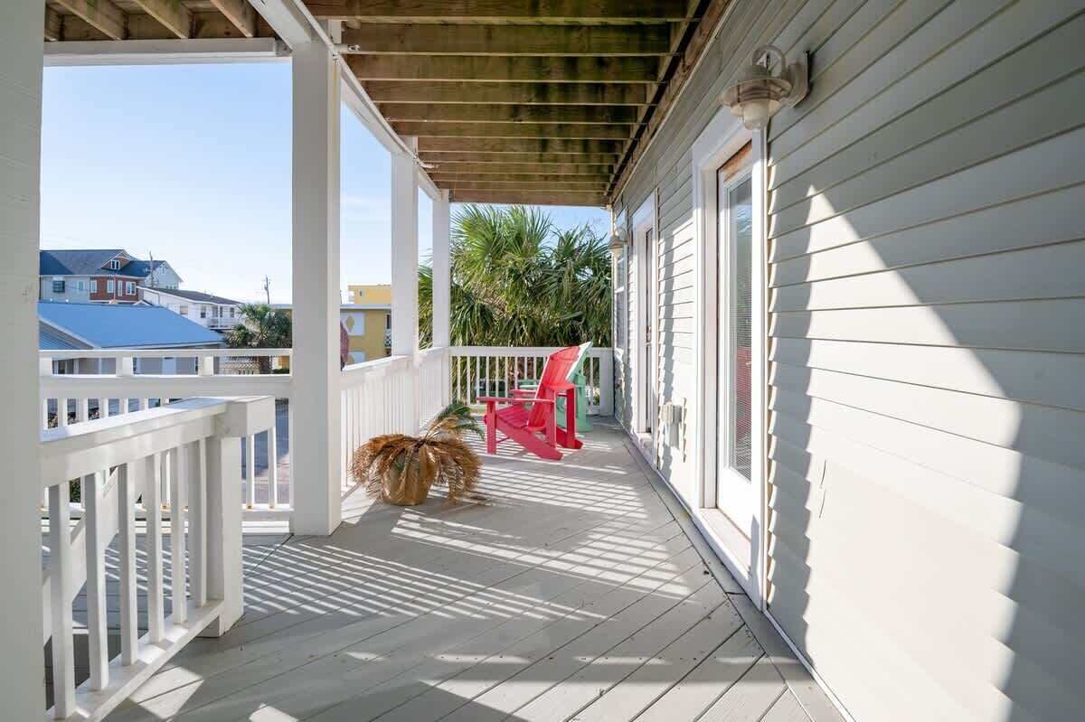 A covered porch with a wooden ceiling, white railings, and a red chair.