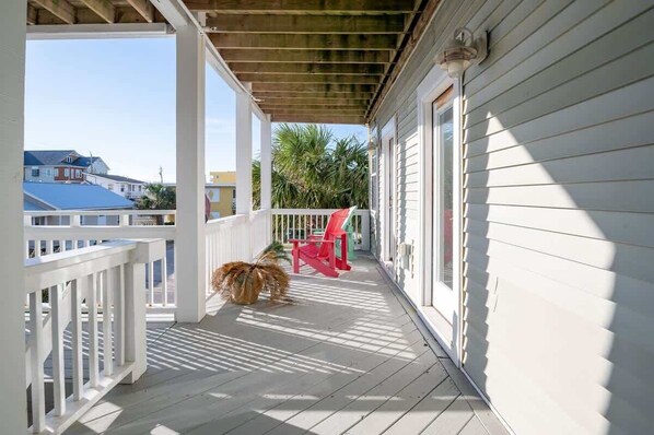 A covered porch with a wooden ceiling, white railings, and a red chair.